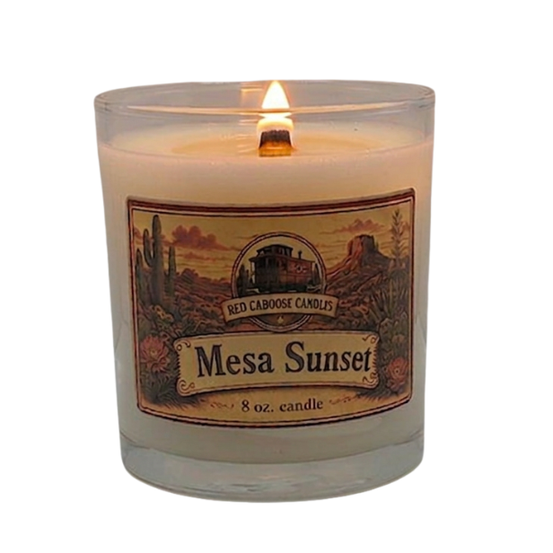A lit 8 oz candle in a clear glass jar with a scenic desert landscape label reading 'Red Canyon Candles Mesa Sunset'.