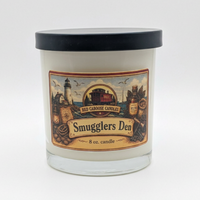 An 8 oz glass jar candle with a black lid and a vintage-style label reading 'Red Ghost Candles' and 'Smugglers Den'.