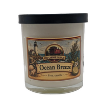 An 8 oz glass jar candle with a black lid and a detailed 'Ocean Breeze' label by Red Caboose Candles, featuring a lighthouse and nautical illustration.